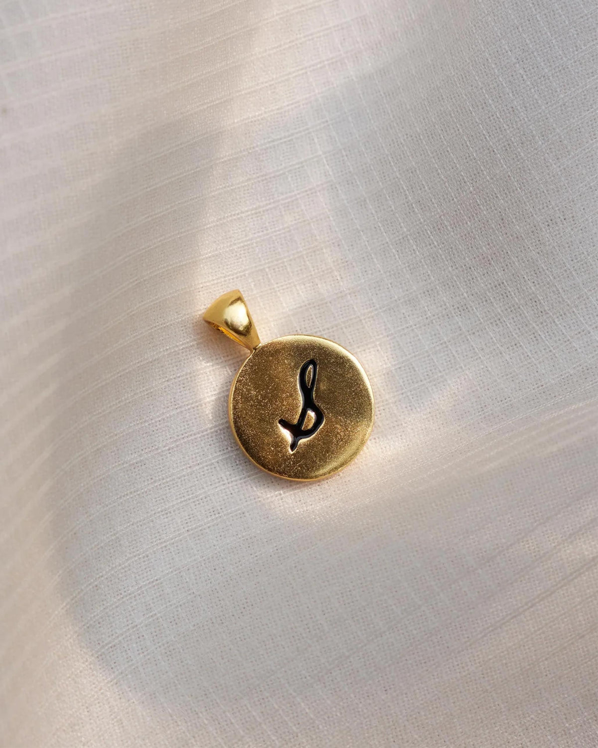Close-up of a gold alphabet charm with a black calligraphic letter.