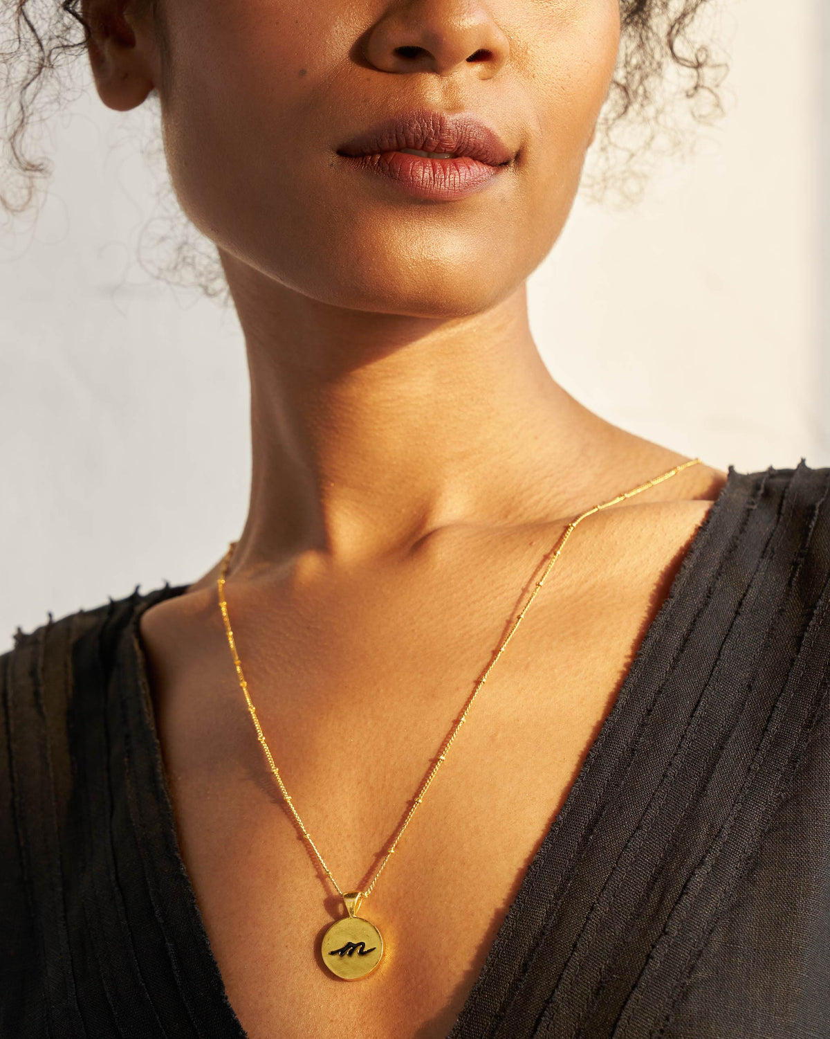 Alphabet M charm with a black script m worn on a gold chain.