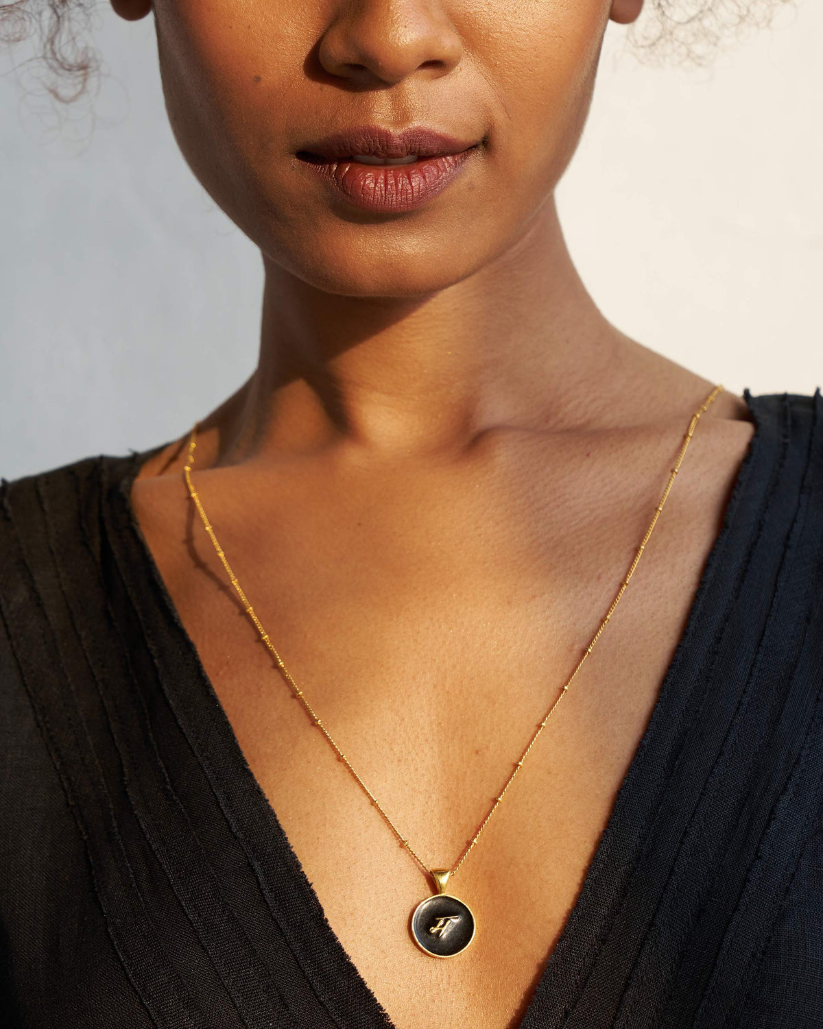 Alphabet M charm in gold and black enamel on a fine chain.