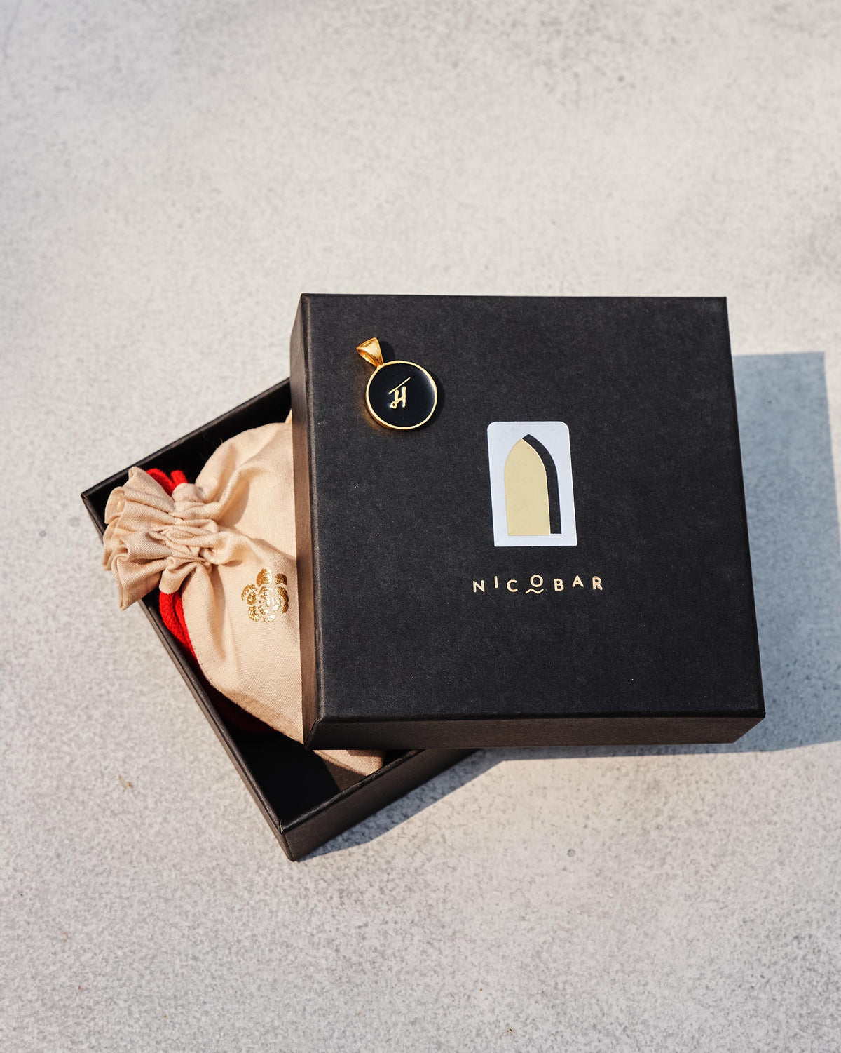 Alphabet M charm in black and gold on a Nicobar gift box.