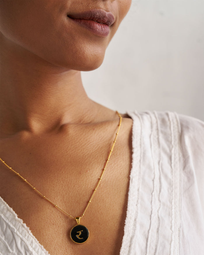 Black and gold Alphabet R charm with र worn on a satellite chain.