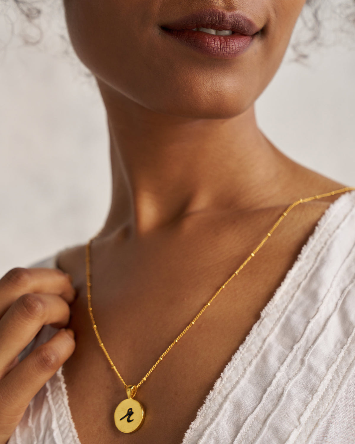 Gold Alphabet R charm with a black script letter r when worn.