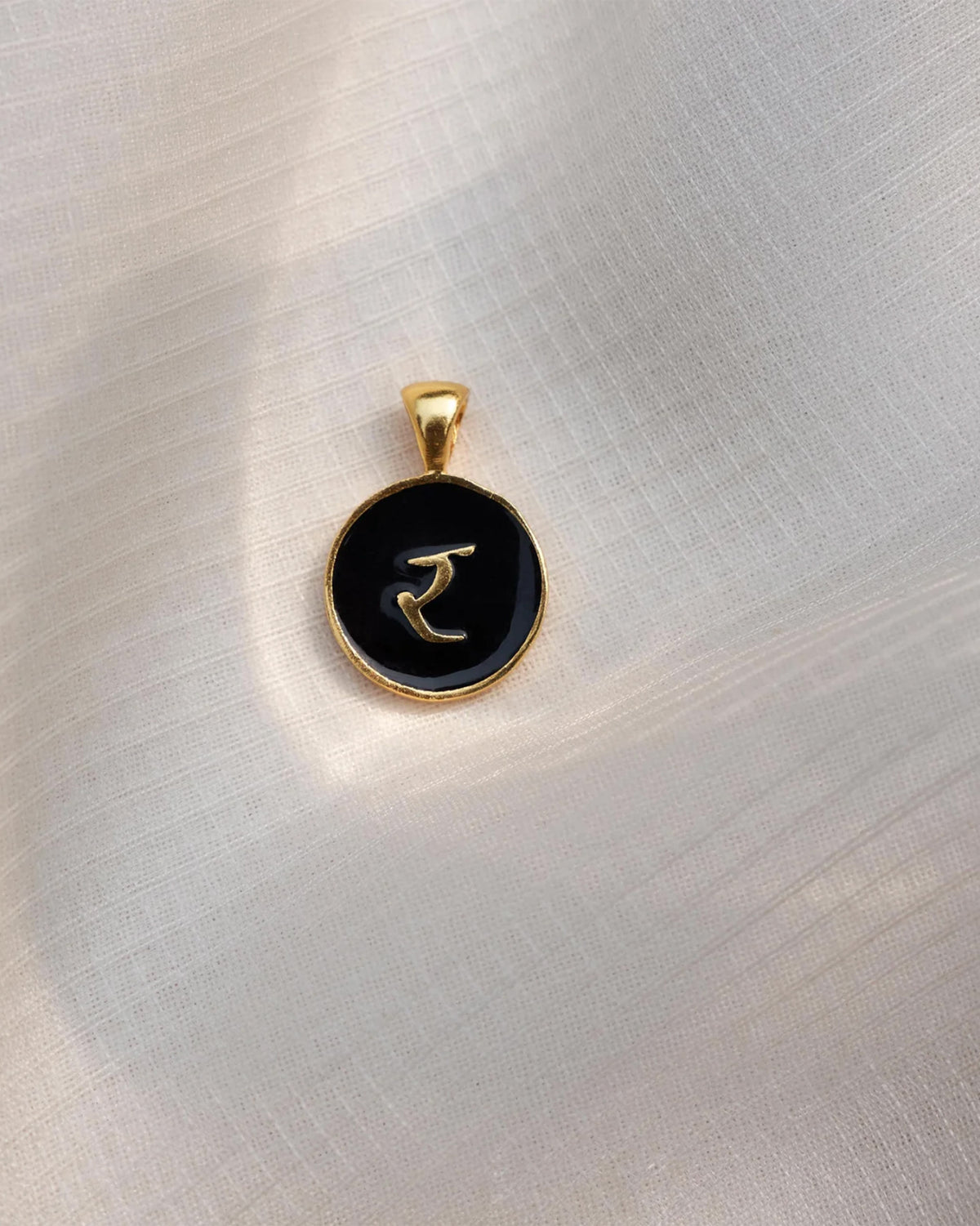 Close-up of a black and gold Alphabet R charm showing र.