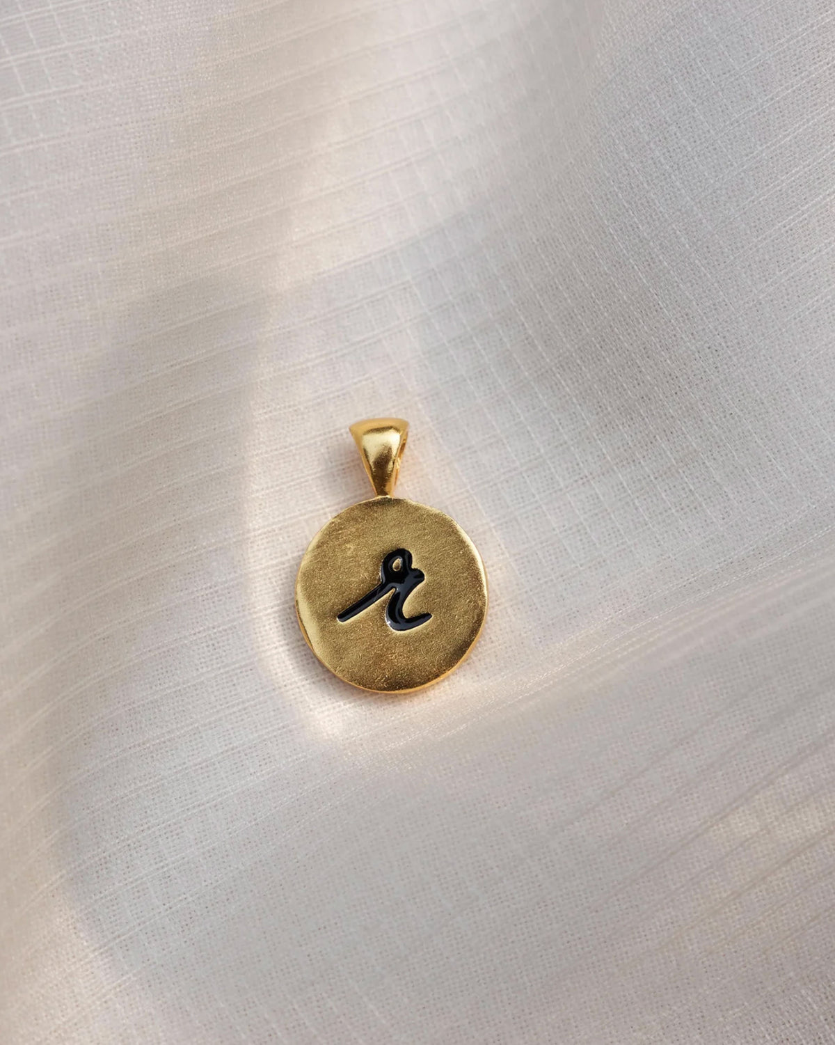 Close-up of a gold Alphabet R charm with a black script r.