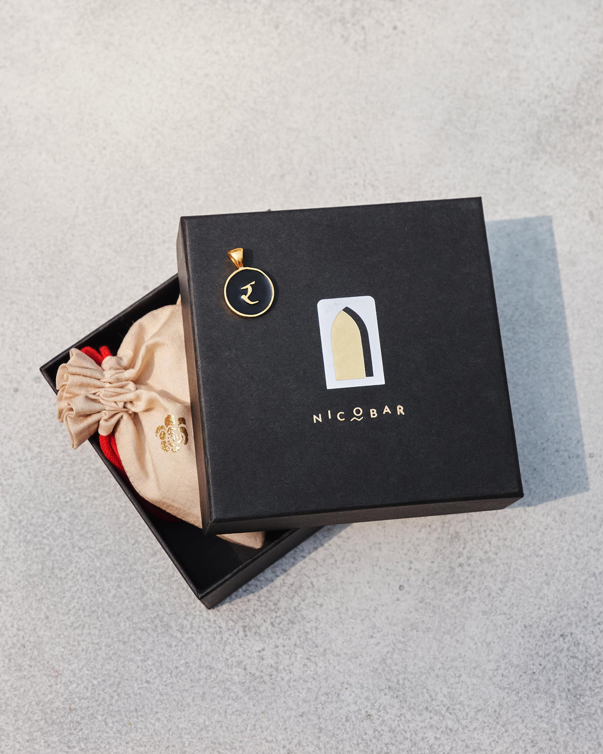 Black and gold Alphabet R charm with र on a Nicobar gift box.