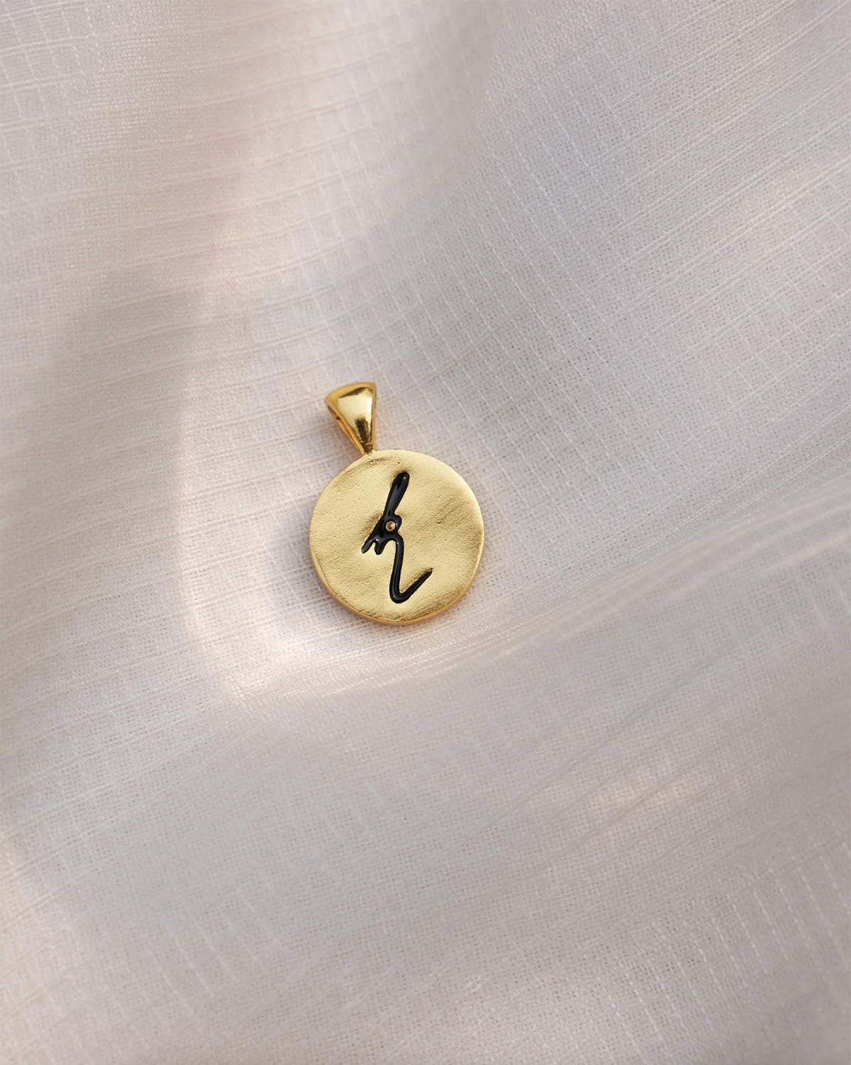 Close-up of a gold Alphabet K charm with a black script k.