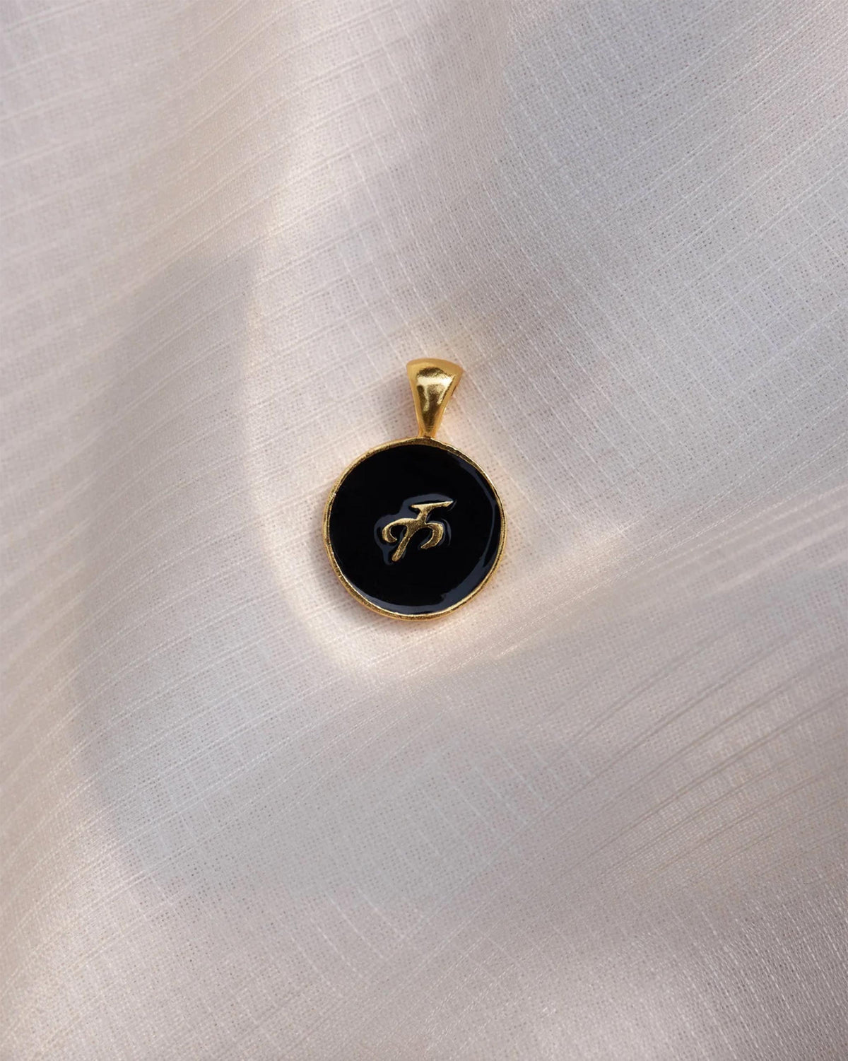 Close-up of a black and gold Alphabet K charm showing क.