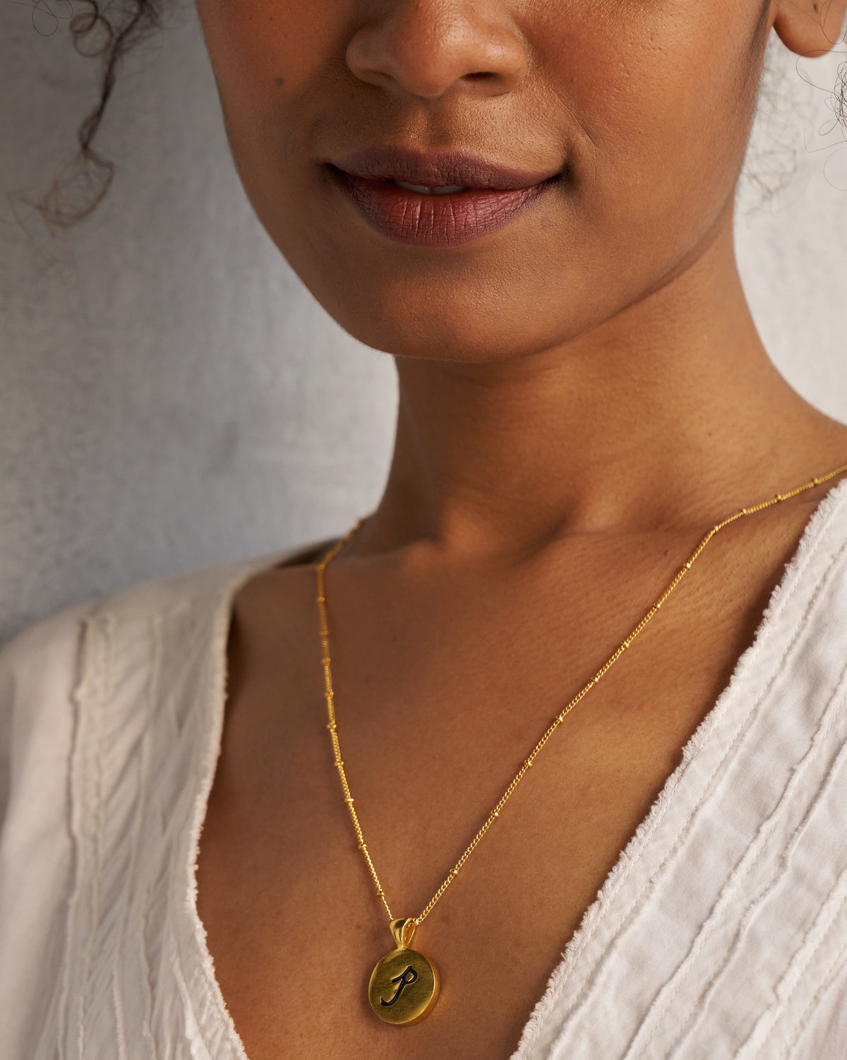 Gold Alphabet P charm with a black script letter p when worn.
