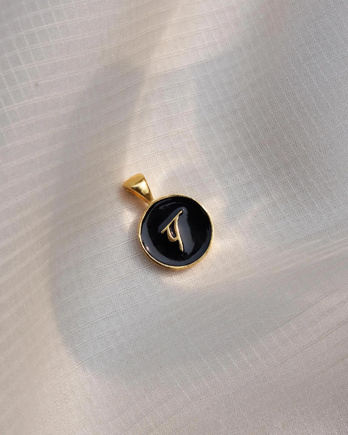 Close-up of a black and gold Alphabet P charm showing प.
