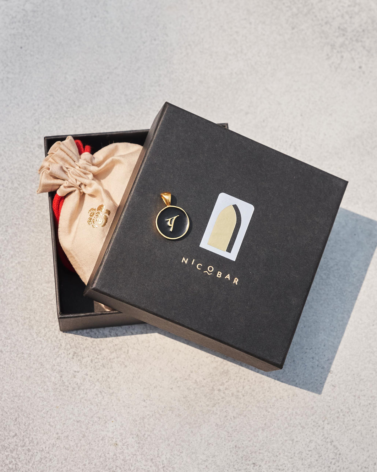Black and gold Alphabet P charm with प on a Nicobar gift box.
