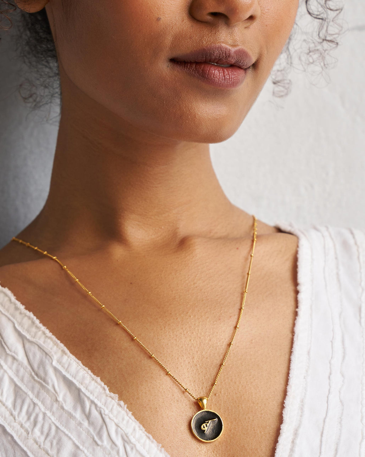 Alphabet B charm in black and gold worn on a fine gold chain.