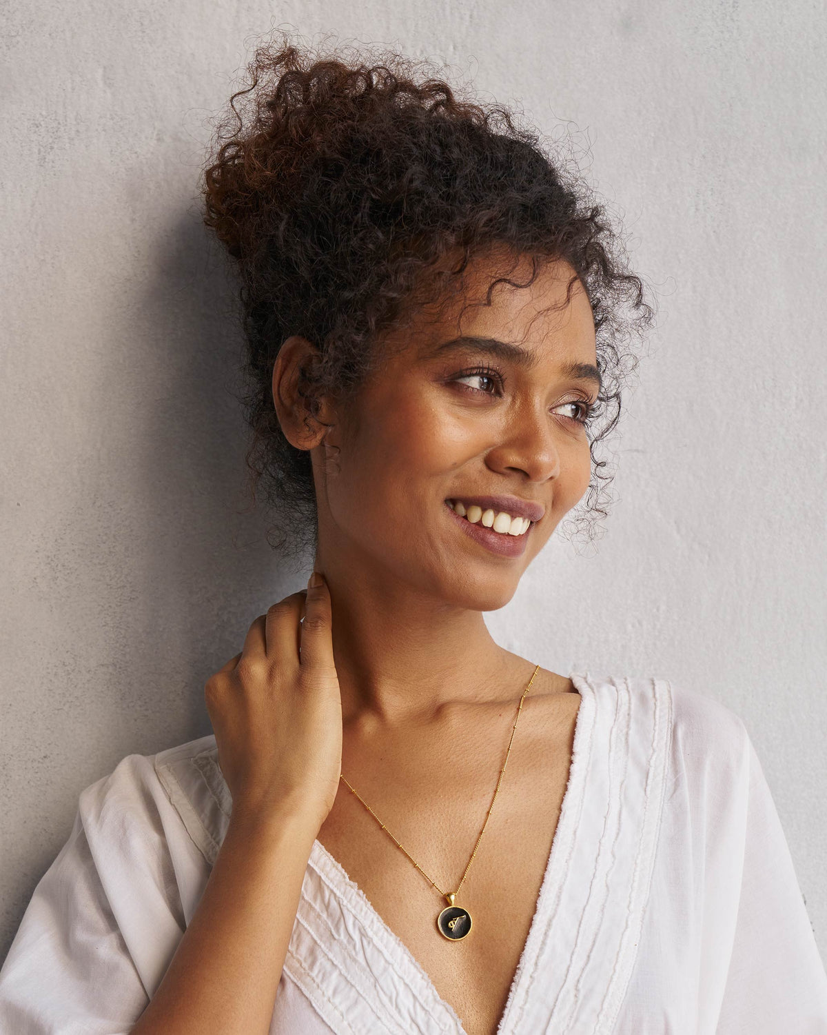 Alphabet B charm worn on a gold chain with a white V-neck top.