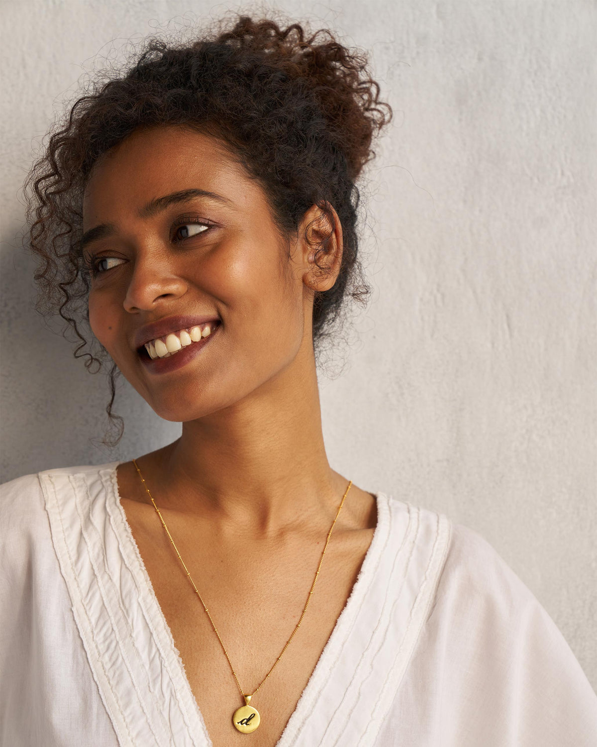 Alphabet D charm worn on a gold chain with a white V-neck top.