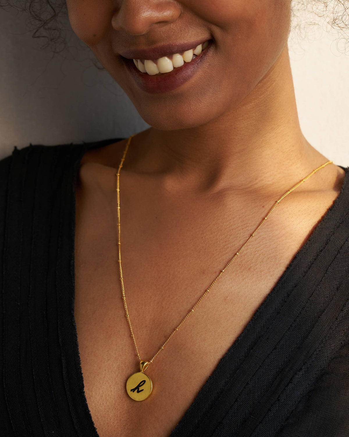 Gold Alphabet H charm with a black script letter h when worn.