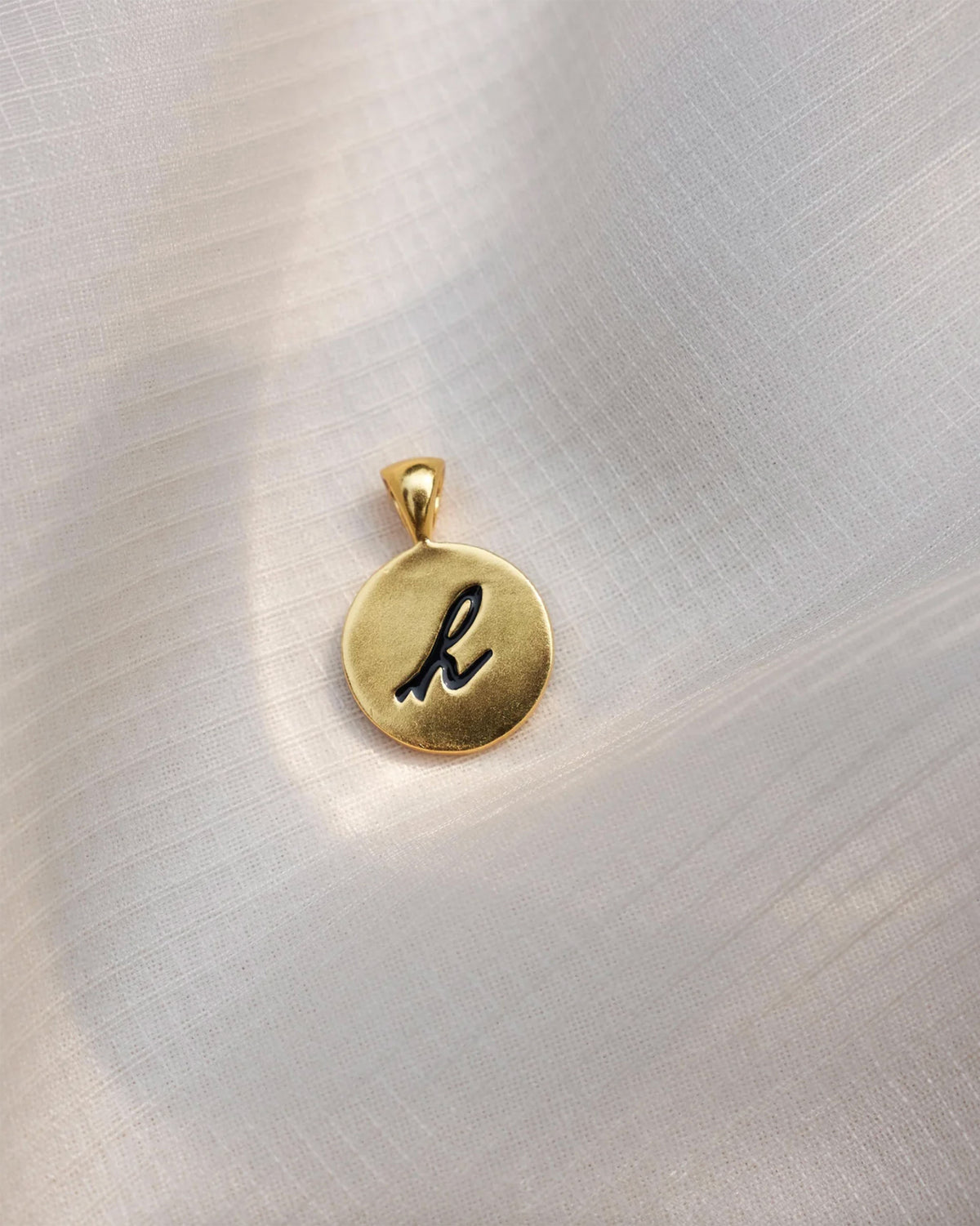 Close-up of a gold Alphabet H charm with a black script h.