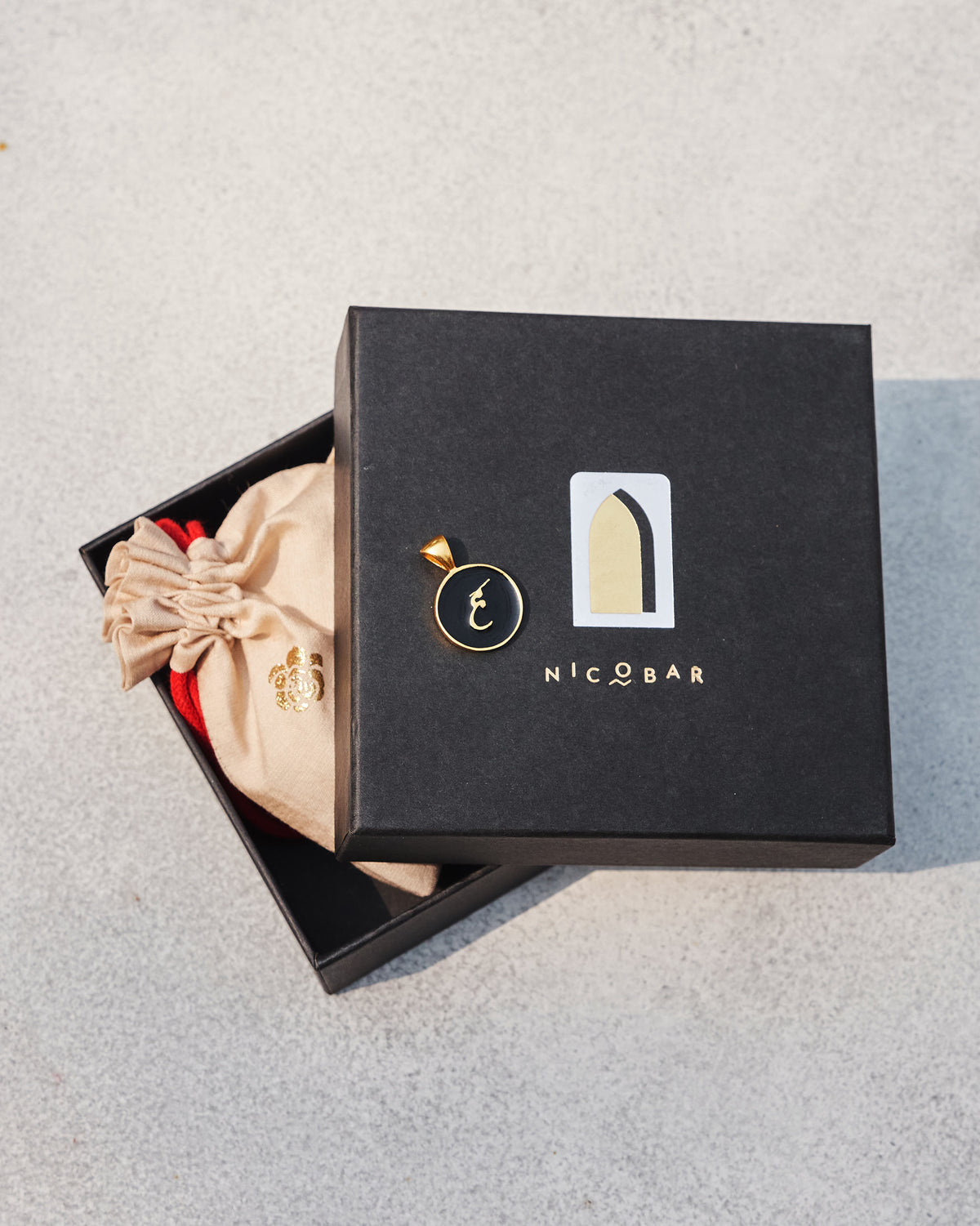 Black and gold Alphabet H charm on a Nicobar gift box.