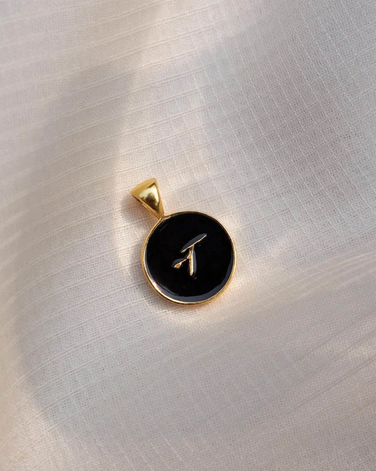Close-up of a black and gold Alphabet N charm showing a Devanagari letter.