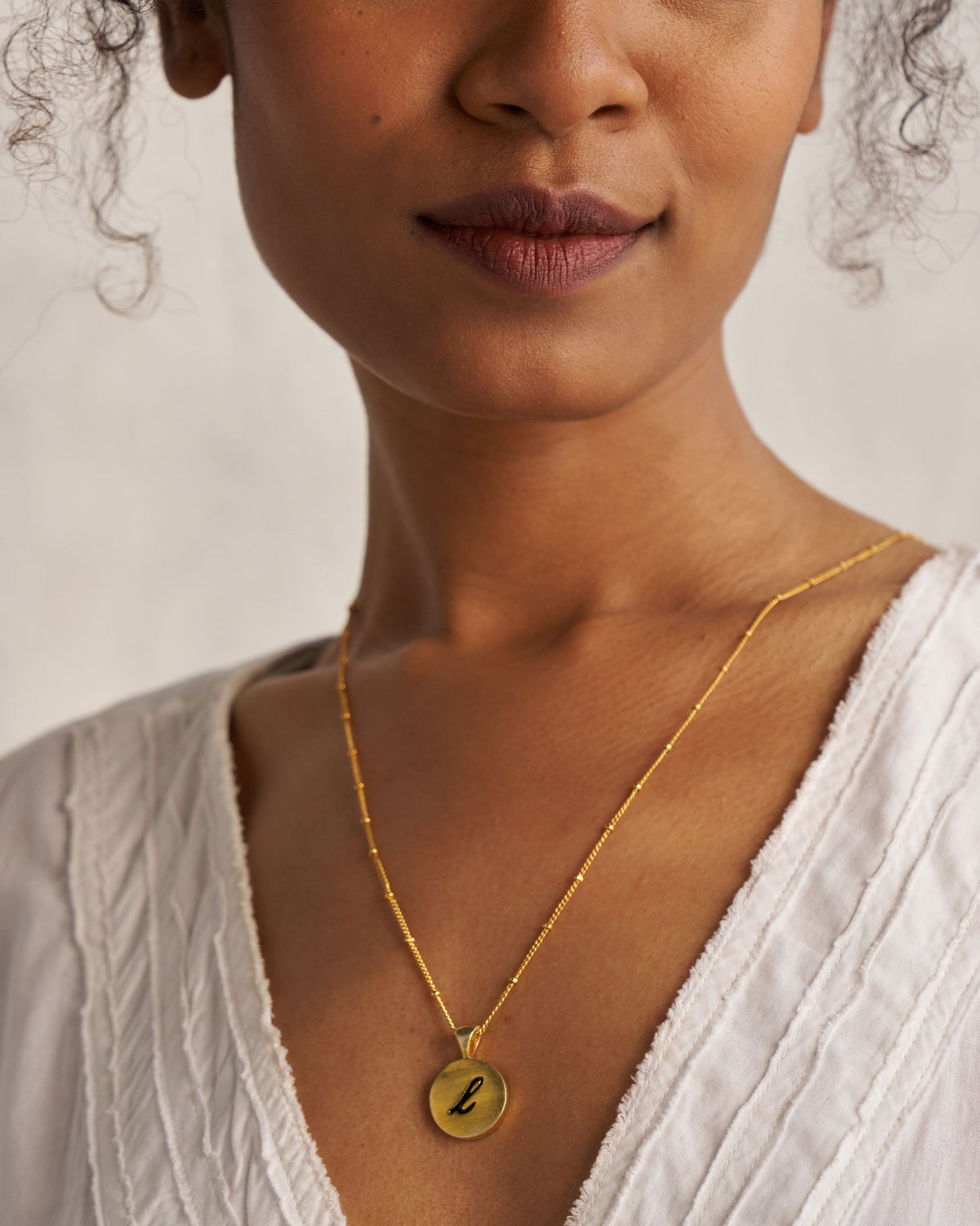 Gold Alphabet L charm with a black script letter l when worn.