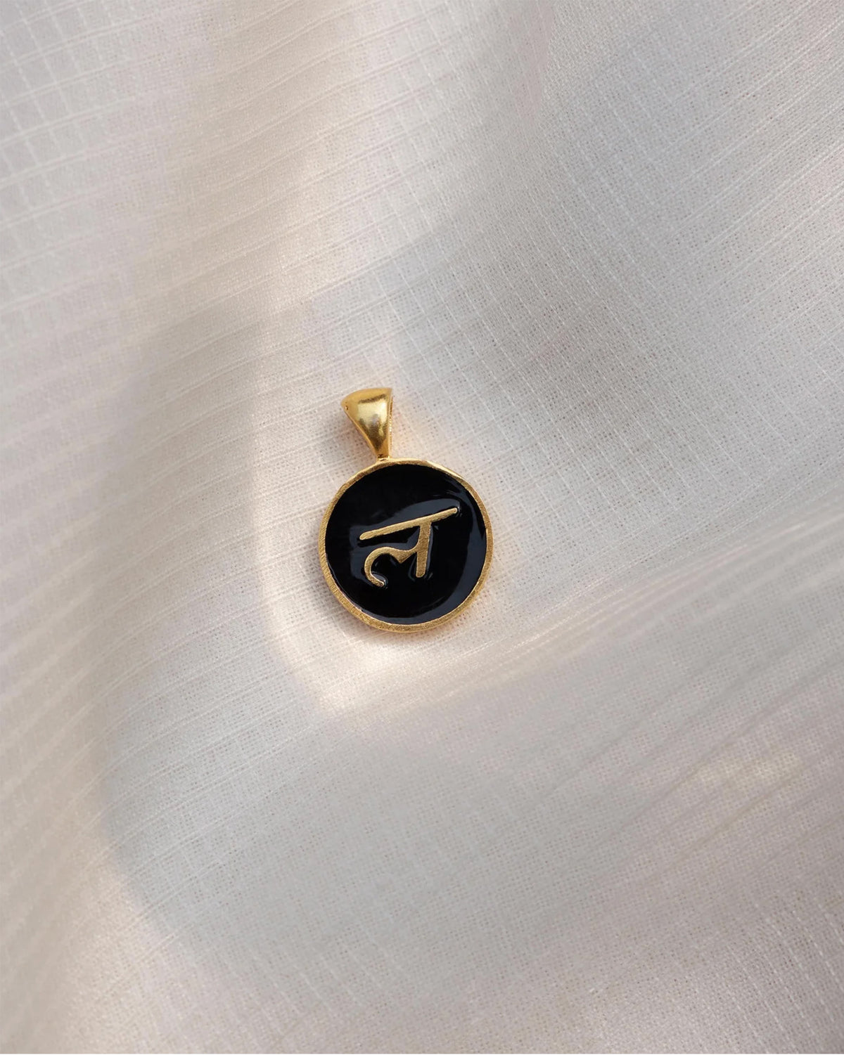Close-up of a black and gold Alphabet L charm showing ल.