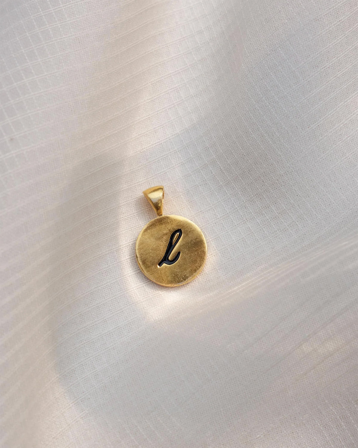 Close-up of a gold Alphabet L charm with a black script l.