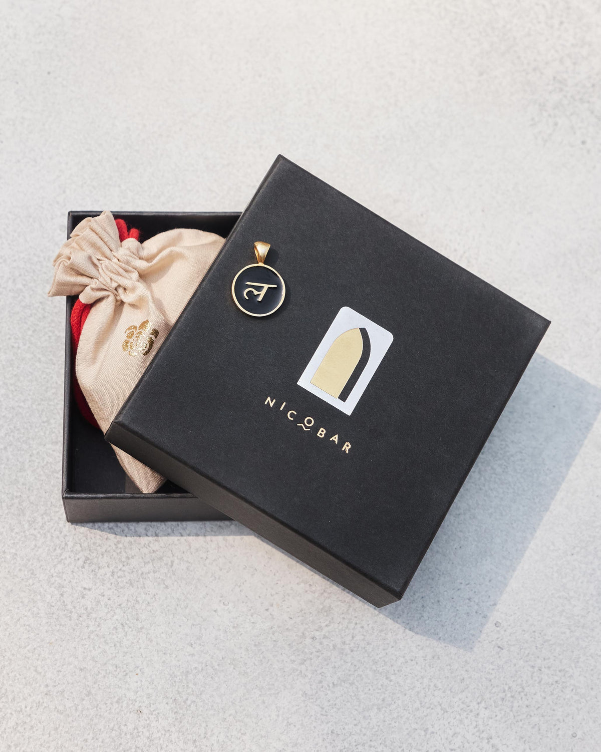 Black and gold Alphabet L charm with ल on a Nicobar gift box.