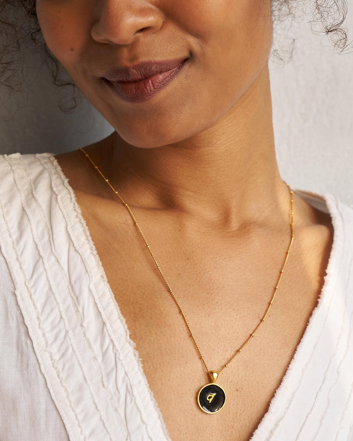 Black and gold Alphabet V charm with व worn on a satellite chain.