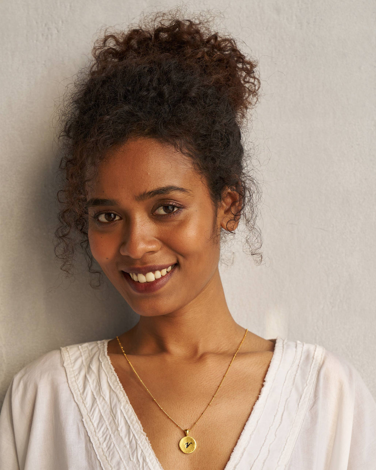 Person wearing a gold Alphabet V charm on a fine chain.