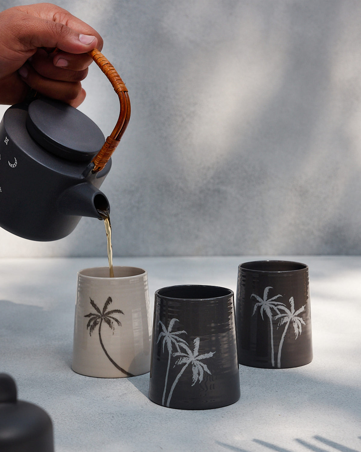 Taramandal charcoal teapot with rattan handle pouring tea into a mug.