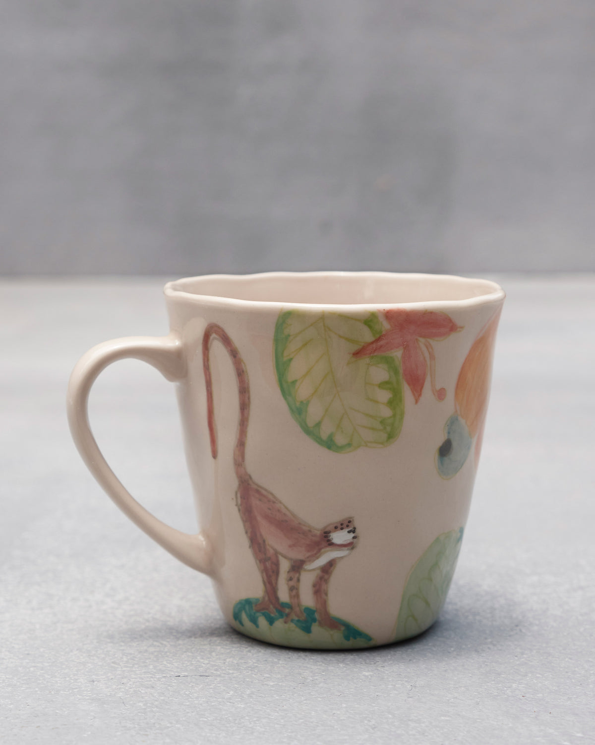 Cream ceramic mug with a macaque, cashew fruit, and tropical leaves.
