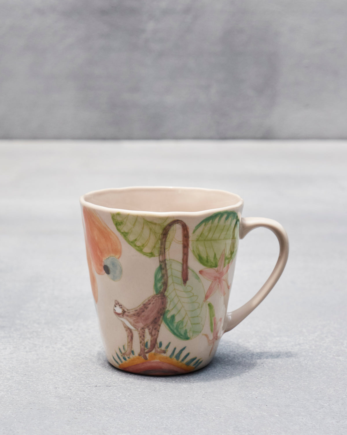 Cream conical mug painted with a macaque, cashew fruit, and pink flowers.