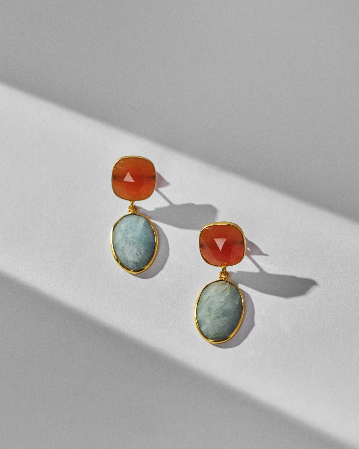 Pair of orange and pale blue icy amber earrings laid flat.