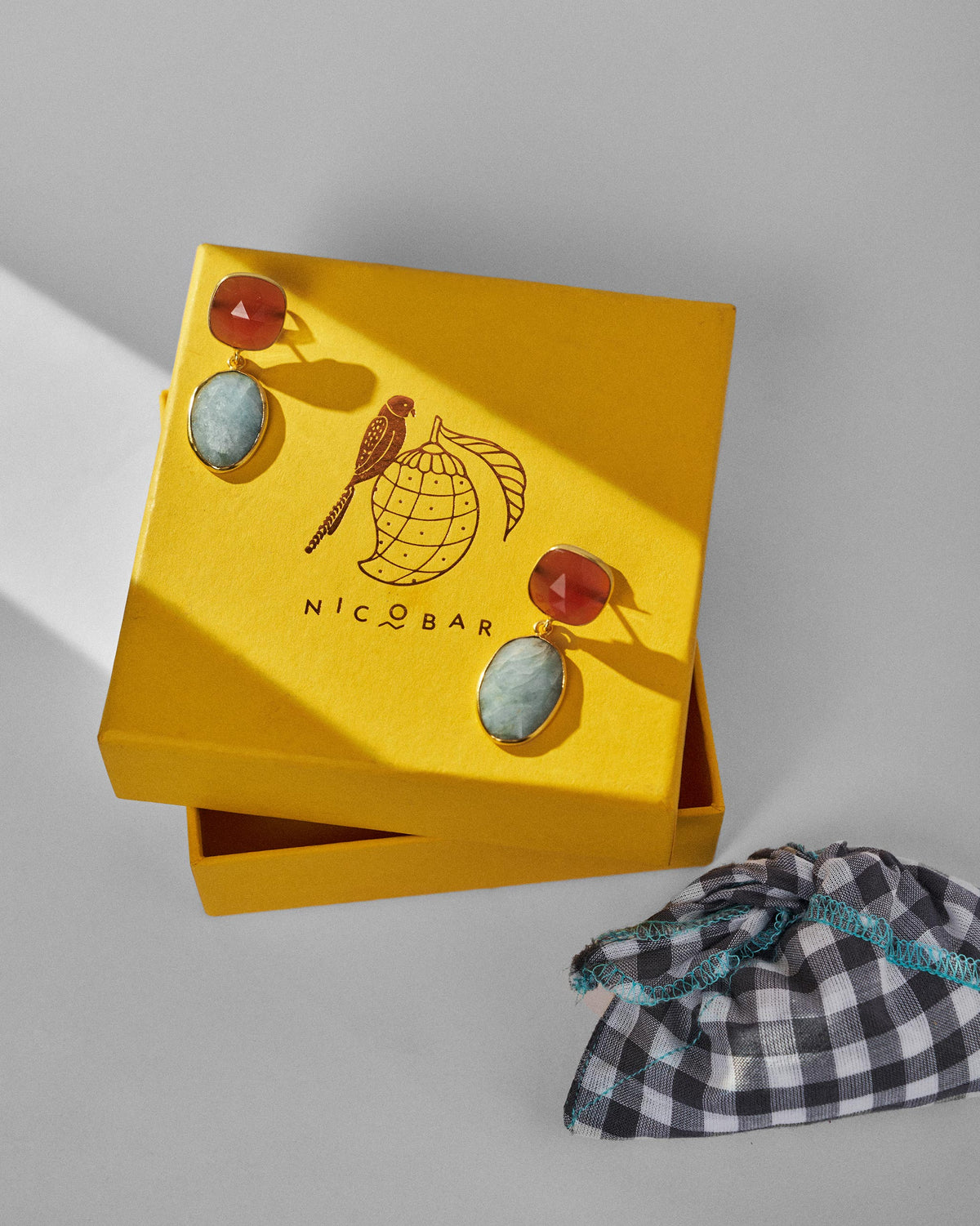 Orange and pale blue icy amber earrings on a yellow Nicobar gift box.