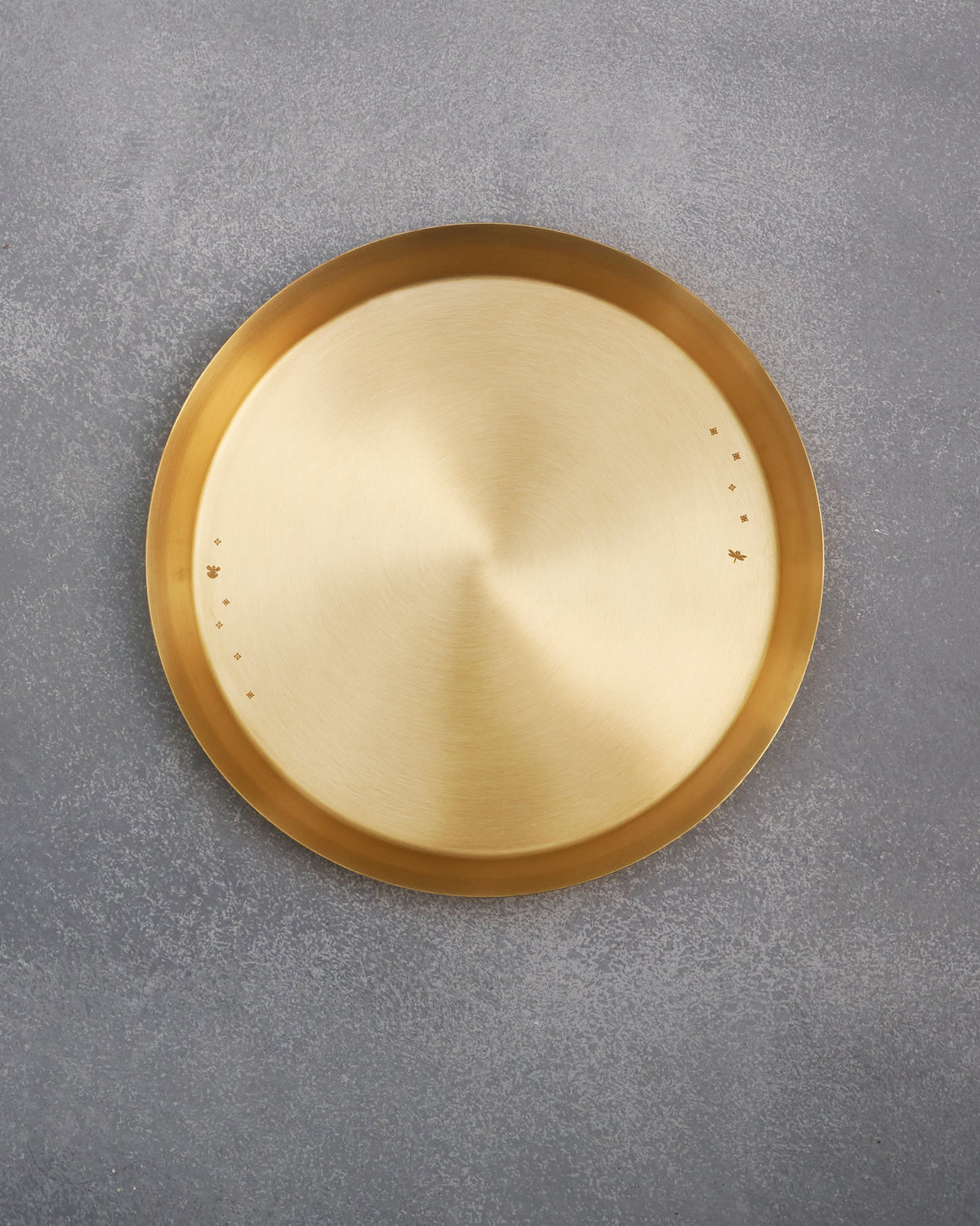 Overhead view of a round brass Madhu thali with rim motifs.