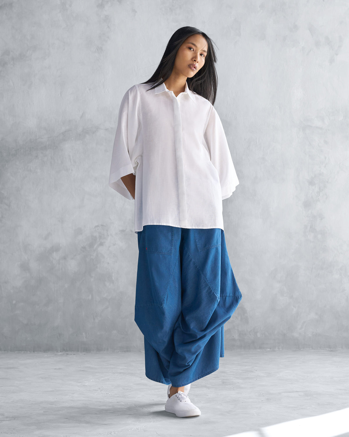 Person wearing a white Drop Armhole Shirt with wide sleeves over blue pants.