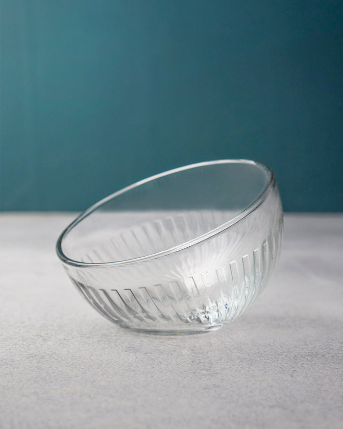 Clear fluted Mahi nut bowl tilted against a teal wall.