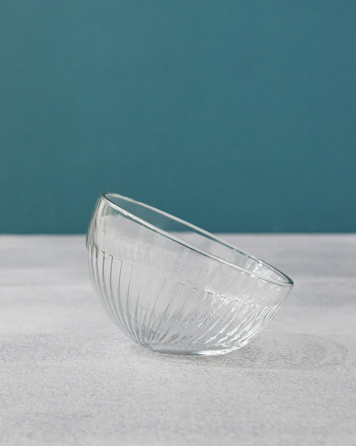 Clear Mahi nut bowl with vertical fluting against a teal background.
