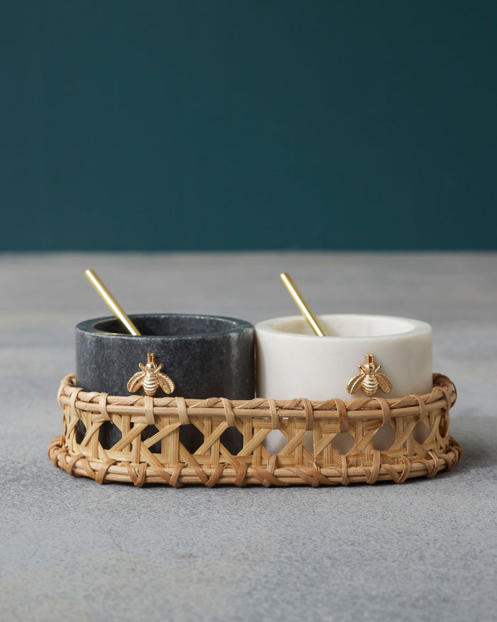Garo salt and pepper pots in black and white marble with gold bee motifs on a rattan tray.