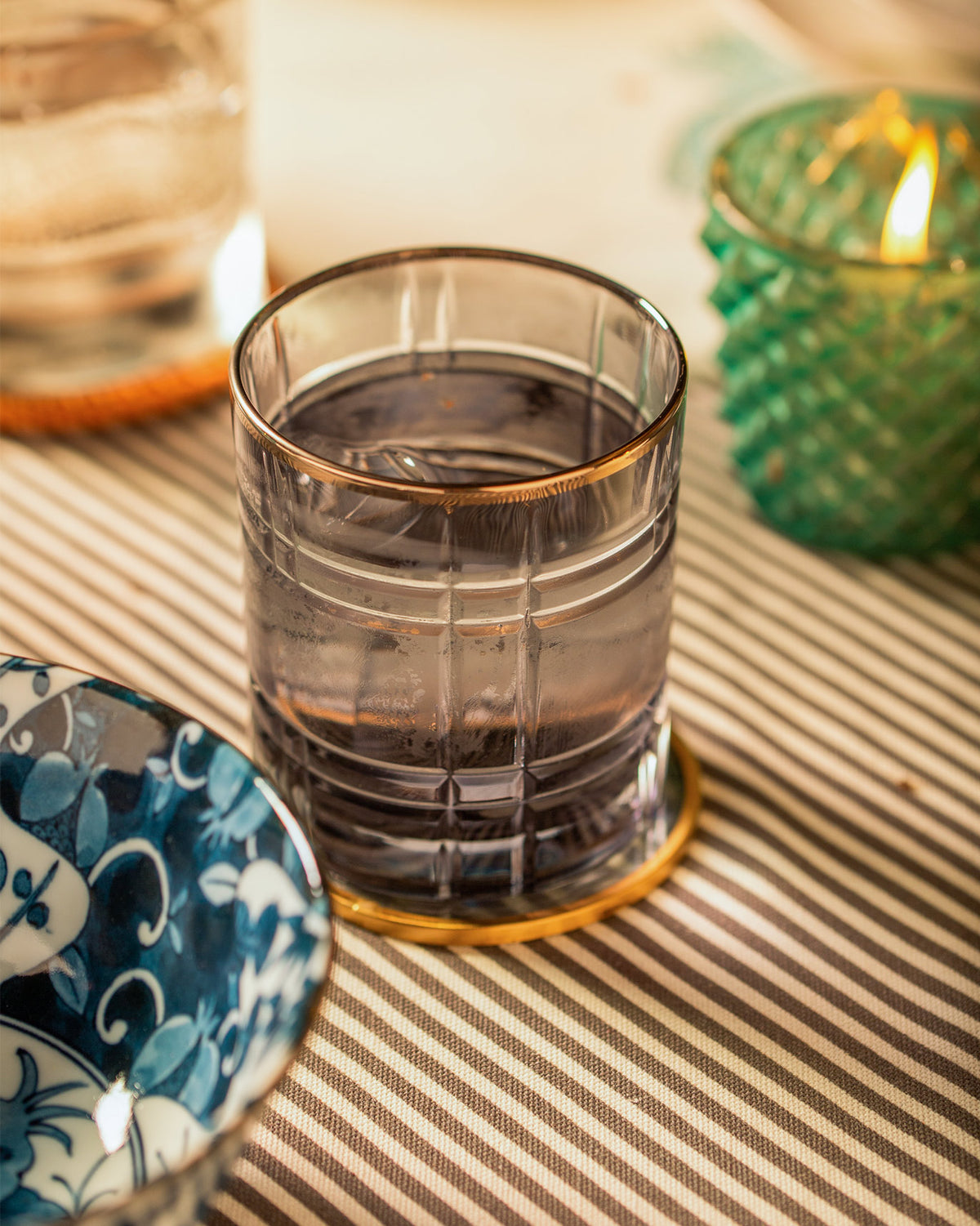 Smoky Celeste whiskey glass with ice on a gold coaster.