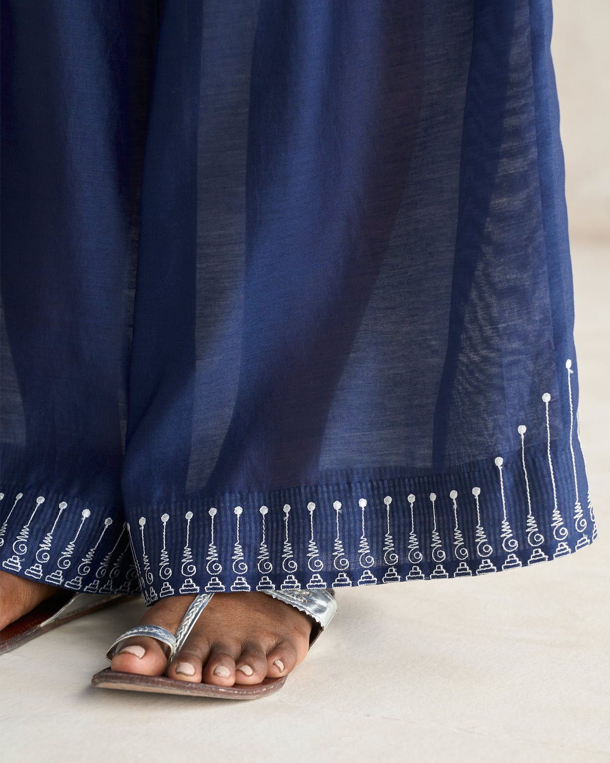 Close-up of the white embroidered hem on navy sheer trousers.