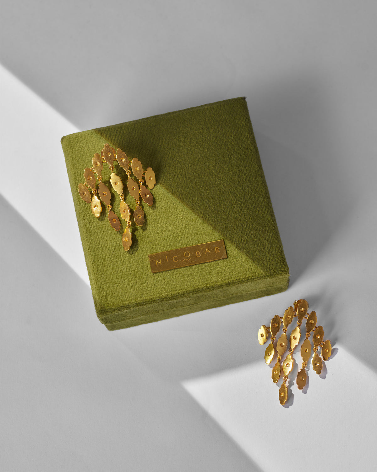 Pair of gold Zedi Drop Earrings displayed on a green Nicobar gift box.