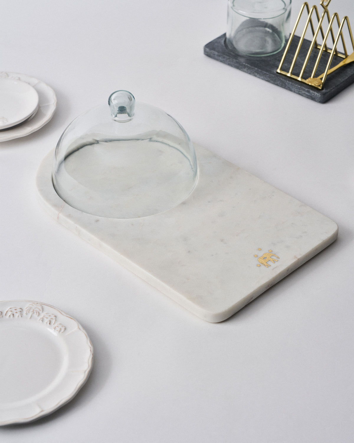 Marble Ele cheese cloche with glass dome set among plates on a dining table.