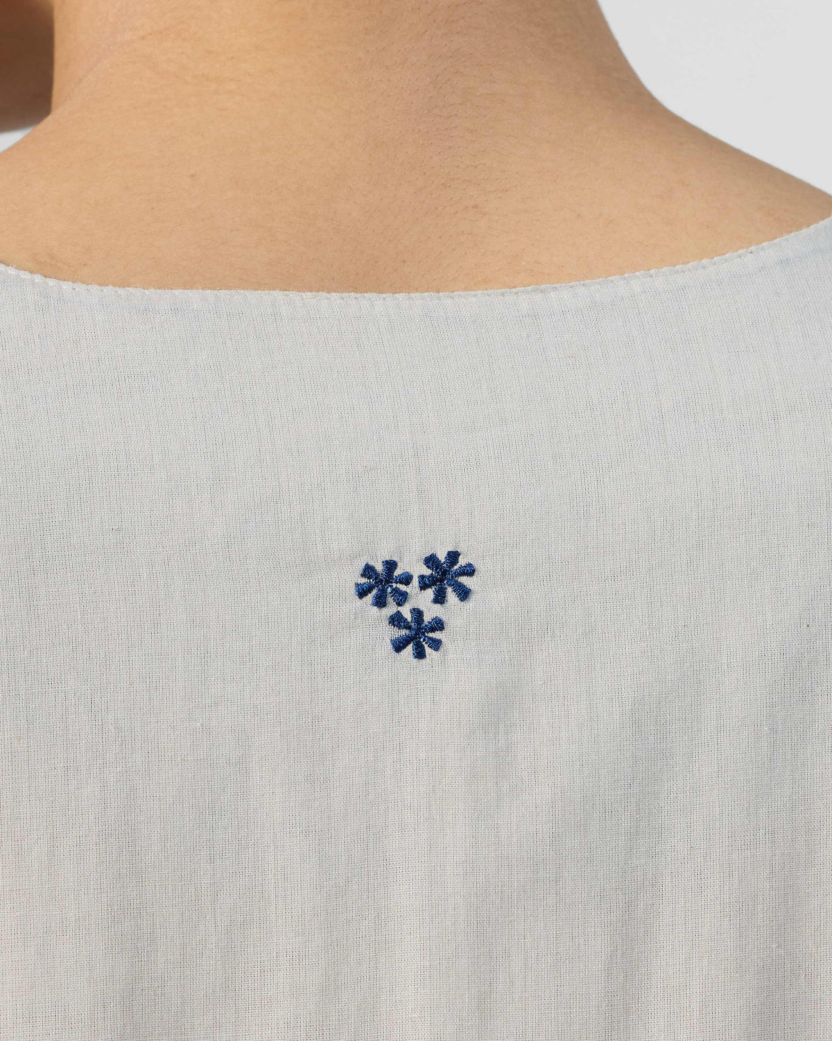 Close-up of blue star embroidery at the back neck of an ivory Temple dress.