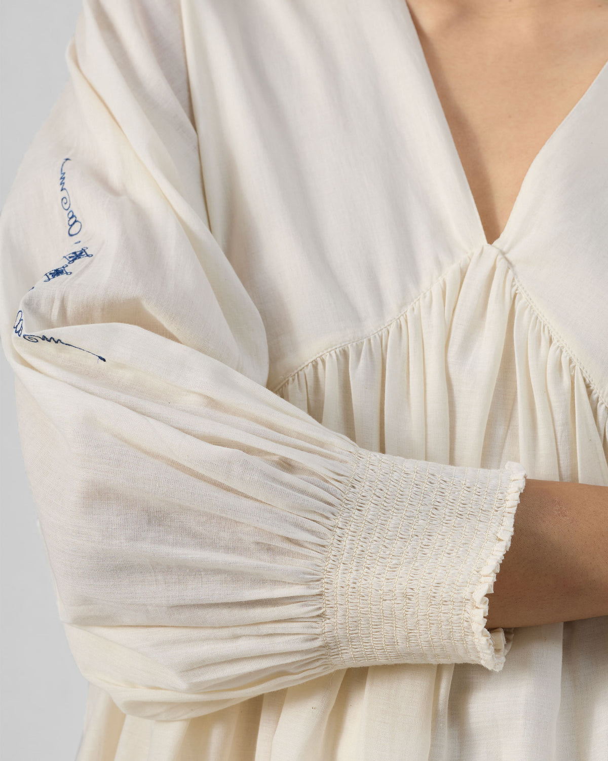 Close-up of the gathered V-neck and smocked cuff on an ivory Temple dress.