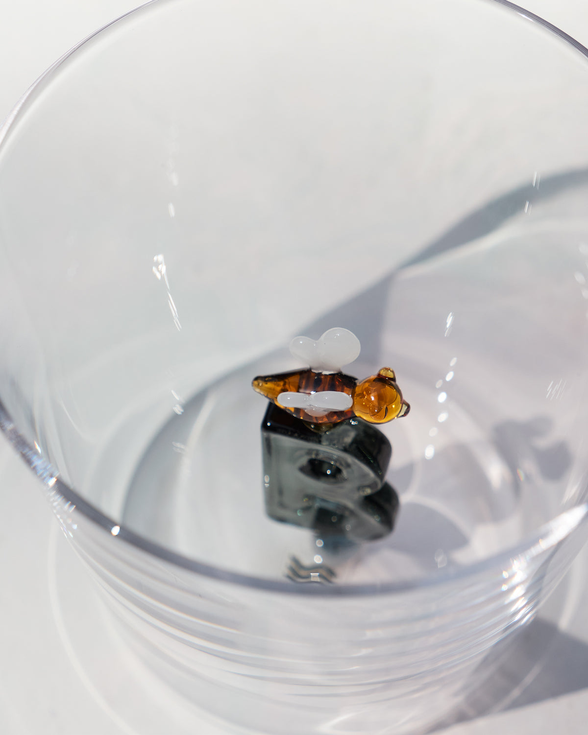 Looking down into a clear glass with a letter B topped by a tiny bee.