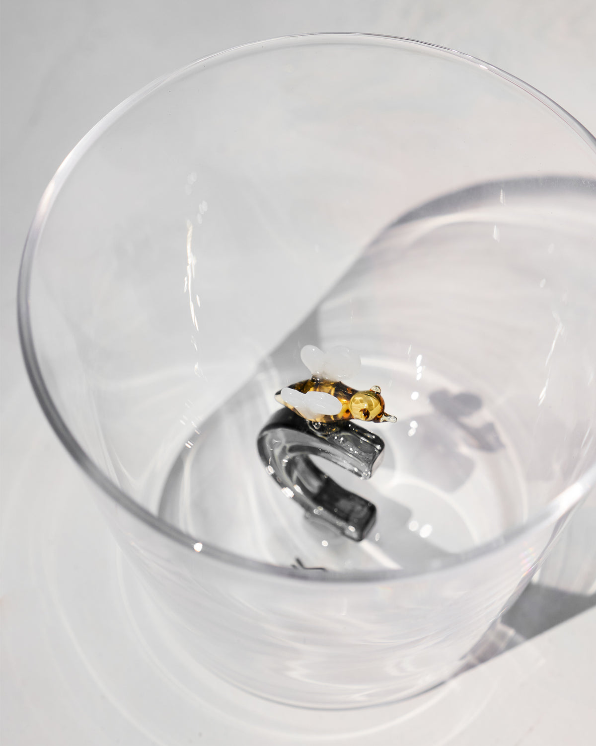 Looking down into a clear glass with a letter C topped by a tiny bee.