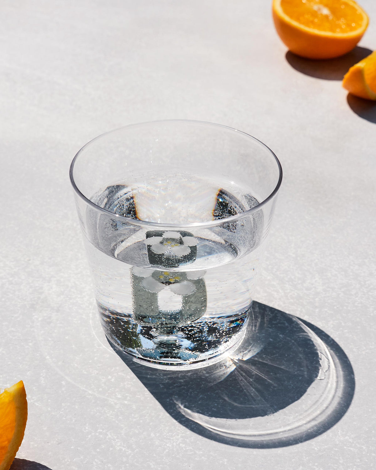Clear Alphabet glass with a white flower at the base, filled with water.