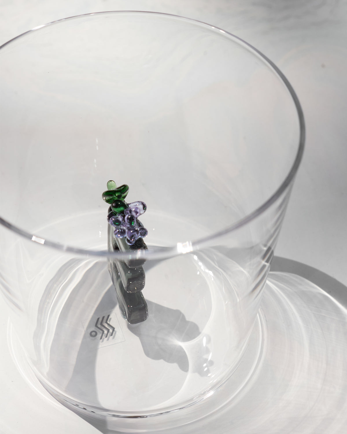 Looking down into a clear glass with purple flowers and a green leaf at the base.