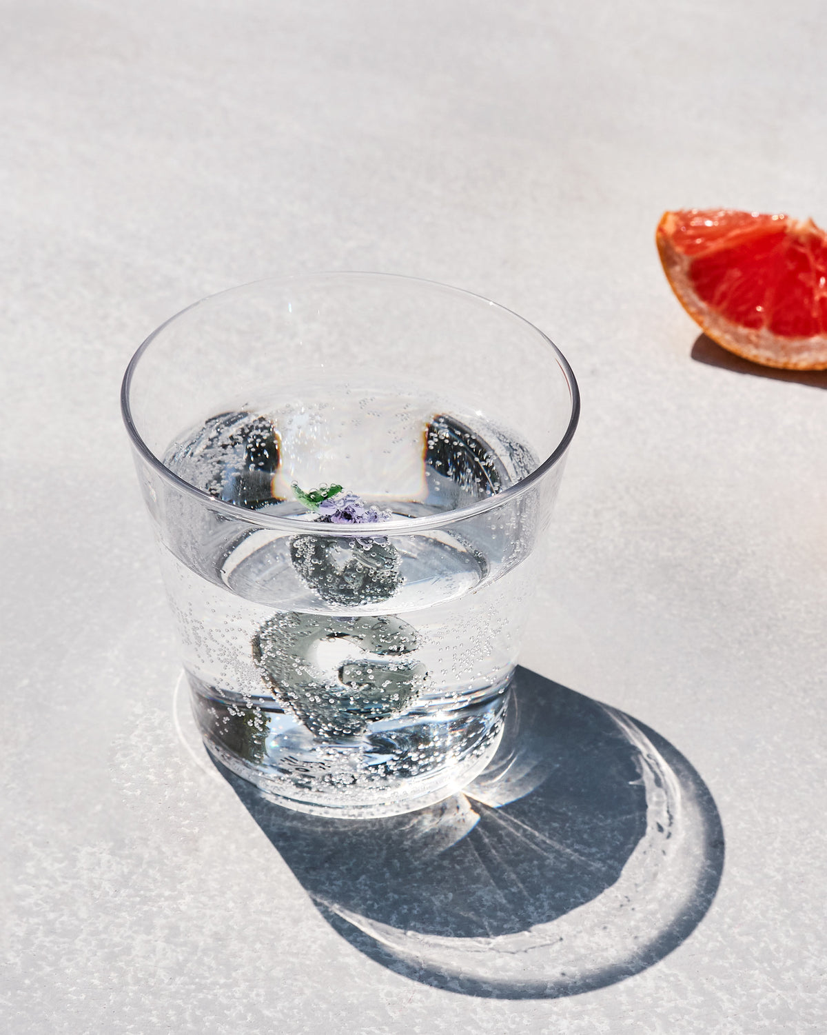 Clear Alphabet glass with purple flowers at the base, filled with sparkling water.