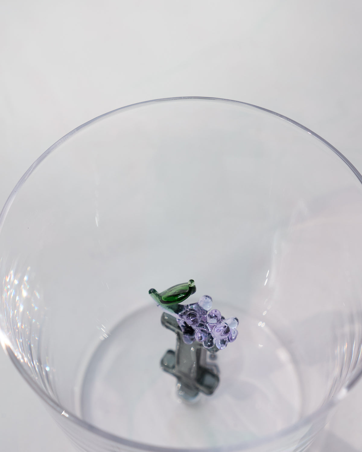 Looking down into a clear glass with purple flowers and a green leaf at the base.
