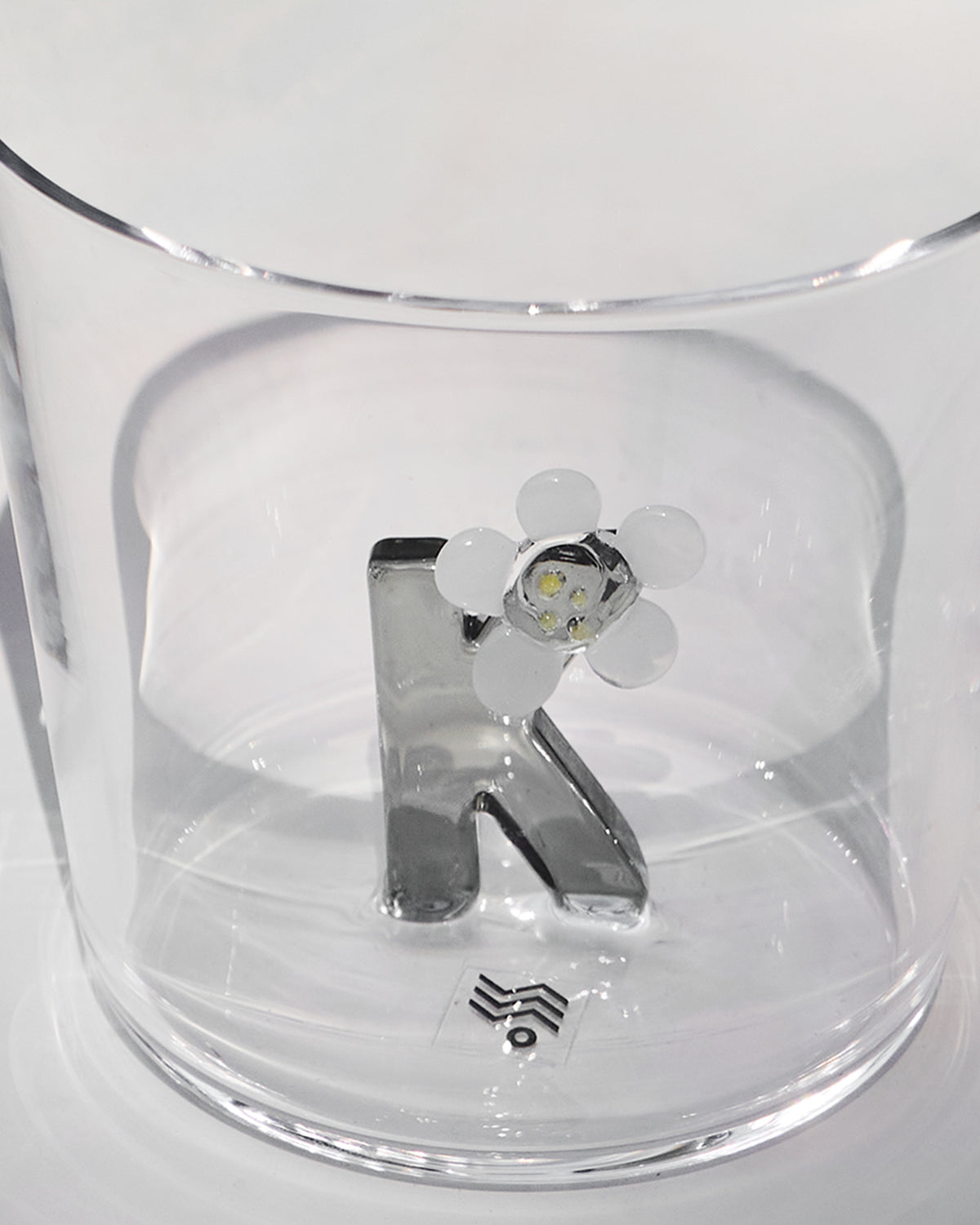 Close-up of a silver letter K with a white flower inside a clear Alphabet glass.